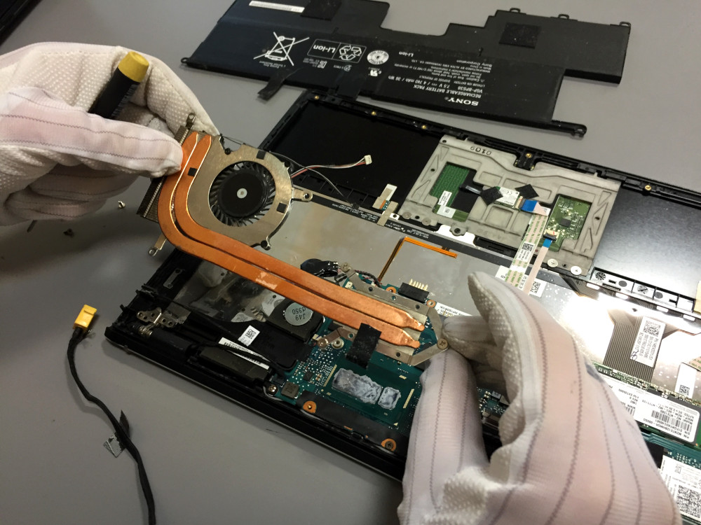 A person uses a can of compressed air to clean dust from the side vent of a laptop, an essential step to help cool down the laptop and improve performance.
