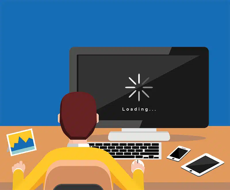 A frustrated person holding their head in their hands while staring at a laptop with a persistent loading symbol on the screen, illustrating the topic of a computer running slowly